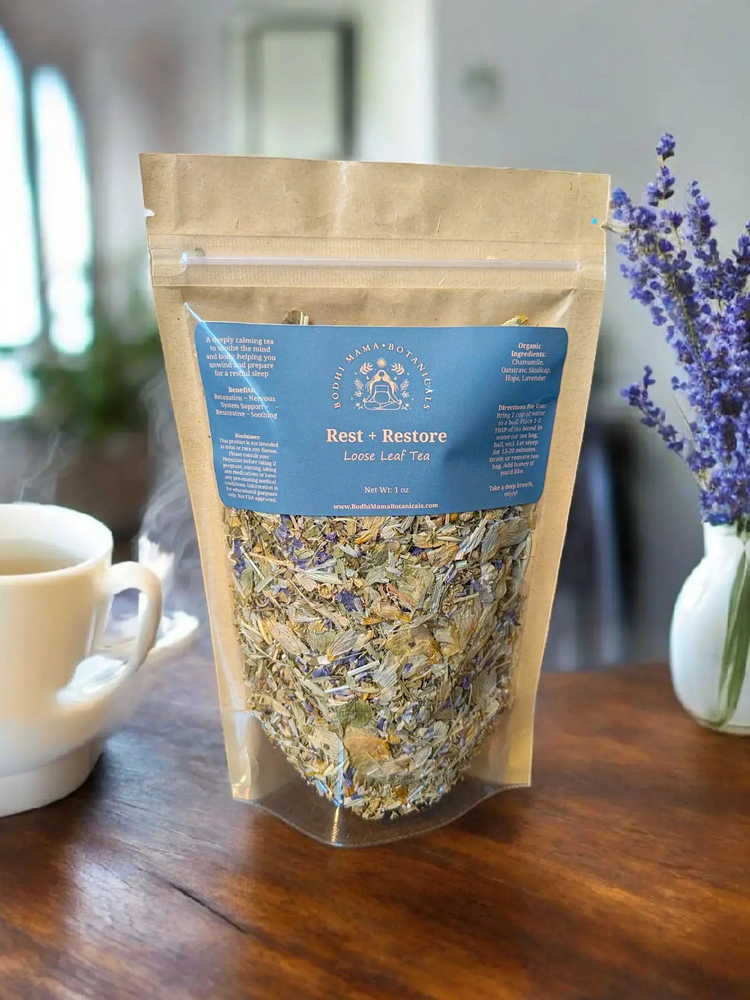Bag of 'Rest + Restore' Loose Leaf Tea on a wooden table with a cup and lavender flowers.